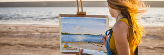 A young woman enjoys her creativity to paint a picture on the beach. Skills she learned in the Hobby Toolbox.